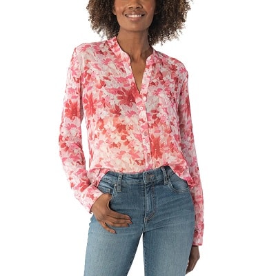 A smiling woman wearing a pink floral print top and jeans 