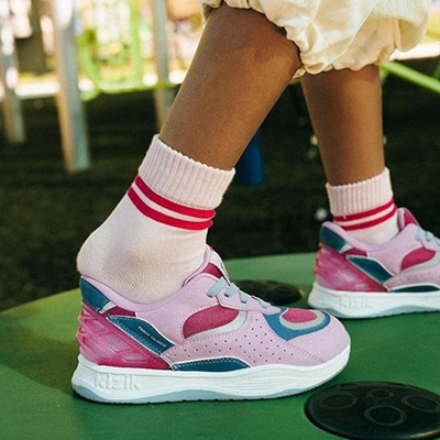 A young girl (only feet and lower legs visible) wearing pink, blue, and white sneakers, with white socks with pink stripes on top