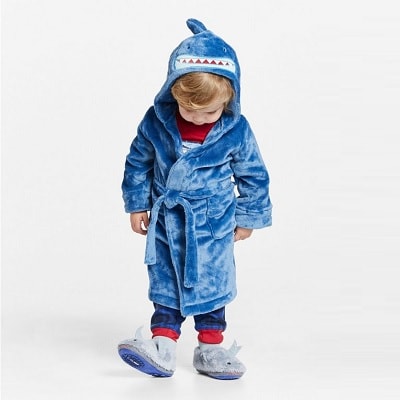 A young boy wearing a blue hooded shark robe and slippers