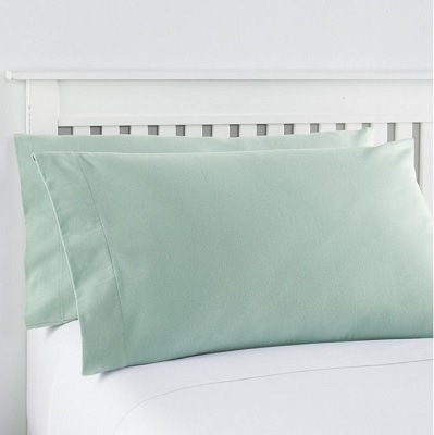 A white bed with two pillows with green pillowcases and white sheets