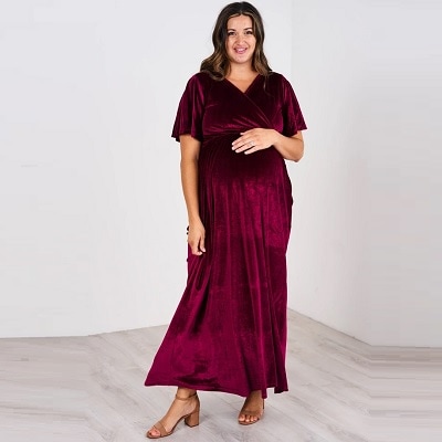 A pregnant white woman with long brown hair wearing a "cranberry"-colored velvet dress