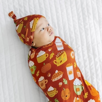 A baby in a fall-themed swaddle and hat