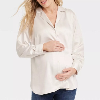 A pregnant woman wearing a white maternity top and blue jeans