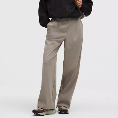 A woman wearing a pair of light brown wide leg trouser pants and multi color sneakers