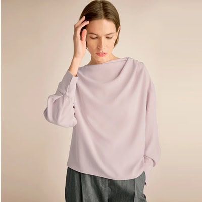 A woman wearing a light lavender draped top with gray pants