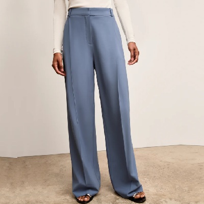 A woman wearing ash blue trouser pants, a white top, and sandals