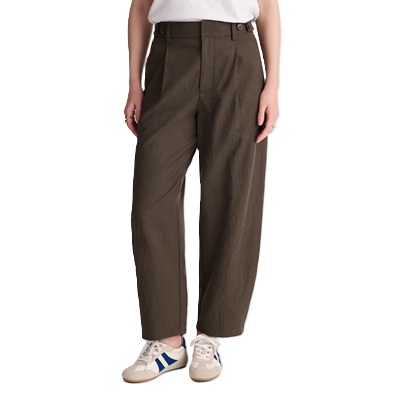 A woman wearing a white top, brown barrel-leg pants, and white/blue sneakers