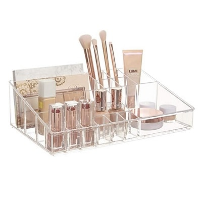 A clear plastic makeup organizer with makeup and makeup brushes in it 