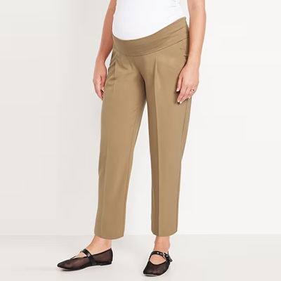 A woman wearing dark khaki maternity pants, a white top, and black flats
