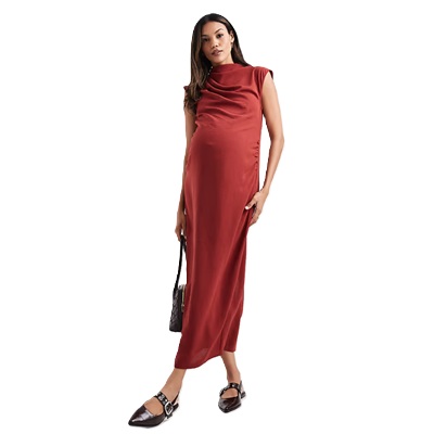 A woman in a rust-colored midi maternity dress with black pointed-toe flats and a black handbag
