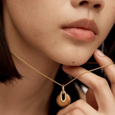 A woman wearing a gold chain necklace with brown gemstone pendant