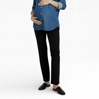 A pregnant woman wearing black flats, black maternity pants, and a blue button-front top