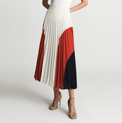 A woman wearing a white top and a midi-length skirt with off-white, red, and black, wearing tan sandals
