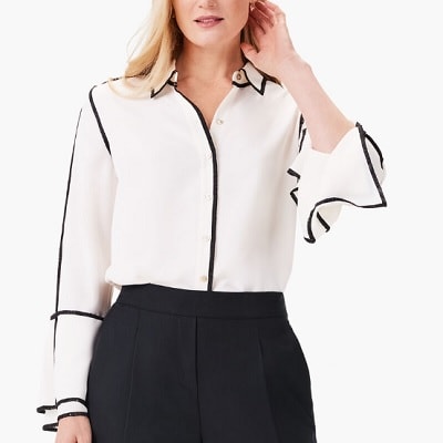 A woman wearing a white blouse with black trim with black pants