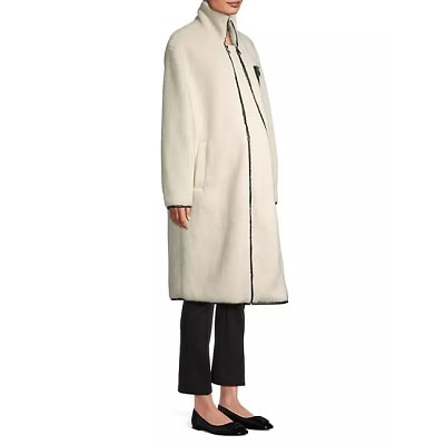 A woman wearing a cream-colored maternity coat, black pants, and black flats
