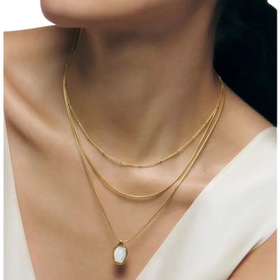 A woman (cropped to only show her neck and collarbones) wearing a white top and gold necklace with moonstone pendant