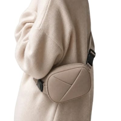 A woman in a beige sweater holding a taupe sling bag