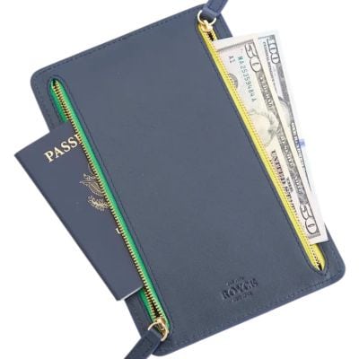 A navy leather travel wallet with a U.S. passport and cash sticking out. The zippers have yellow and green trim.