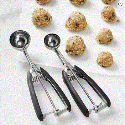 Two metal cookie scoops on a white counter with several balls of cookie dough