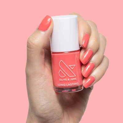 A woman's hand holding a bottle of pink Olive and June nail polish