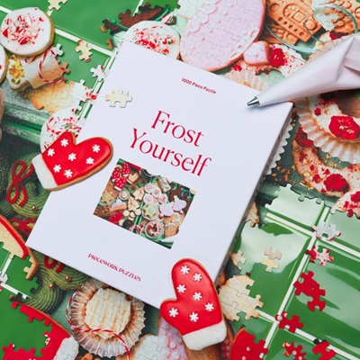 A box for a puzzle called "Frost Yourself," on top of a Christmas tablecloth