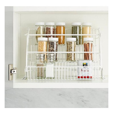 A white wire spice rack, full of spice jars, in a white cabinet