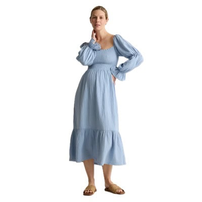 A pregnant woman wearing a light blue smocked midi dress with brown woven sandals