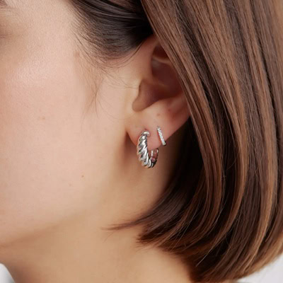 A closeup of the side of a woman's head; she has short brown hair that is tucked behind her ear to show two silver hoop earrings, with the front one larger than the other