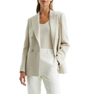 A woman wearing a cream-colored blazer, cream-colored top, and white pants
