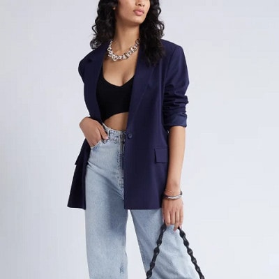 A woman wearing a black crop top, navy blazer, and jeans