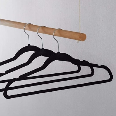 Three black velvet hangers hanging on a wooden rod in front of a white wall