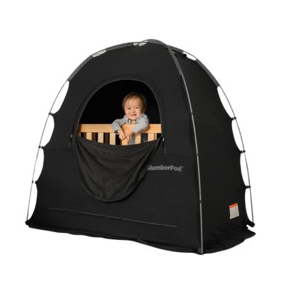 A large black tent surrounding a wooden crib with a toddler standing inside and smiling