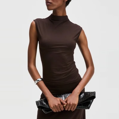 A woman wearing a chocolate brown top and matching skirt, wearing a silver bangle and carrying a black clutch