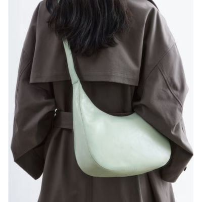 A woman wearing a gray trench coat and carrying a light green handbag