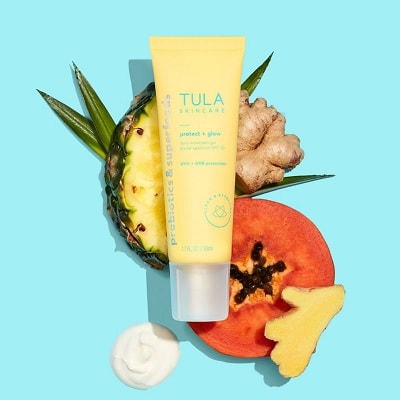 A yellow sunscreen bottle on top of a slice of pineapple, piece of ginger, and slice of papaya