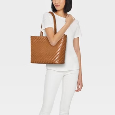 A woman wearing all white and carrying a brown woven tote on her shoulder