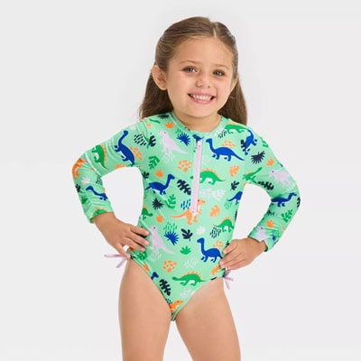 A young girl wearing a long-sleeved green rashguard with a dinosaur print