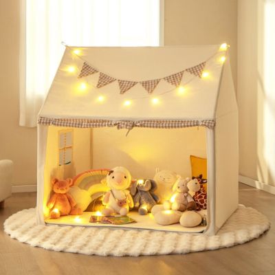 An ivory play tent on top of an ivory round rug. Inside the tent are several stuffed animals and two books. There is a string of lights on top of the tent.