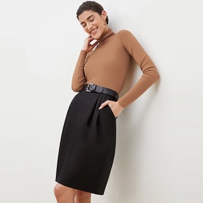 A short-haired, light-skinned woman wearing a camel-colored turtleneck, black skirt, and black belt