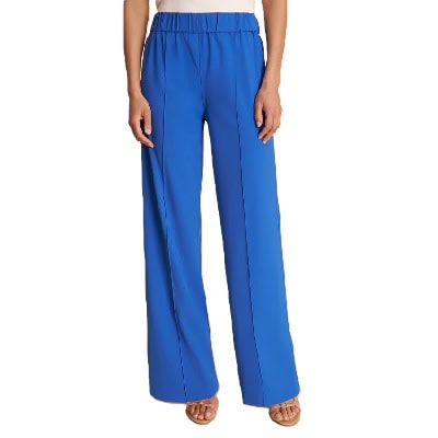 The lower half of a woman; she is wearing a white top and bright blue pants with tan sandals