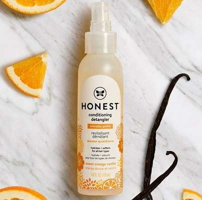 A bottle of Honest Company Conditioning Detangler surrounded by a few orange slices and pieces of vanilla 