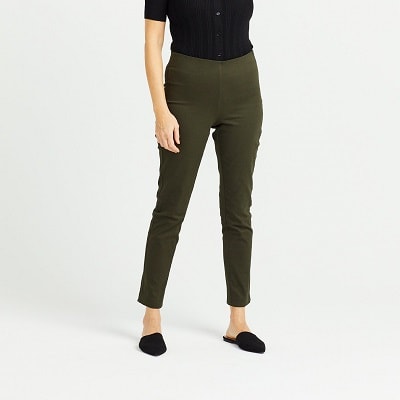 A woman wearing olive colored, tailored pants and a black shirt and black slides (head and shoulders cropped out)