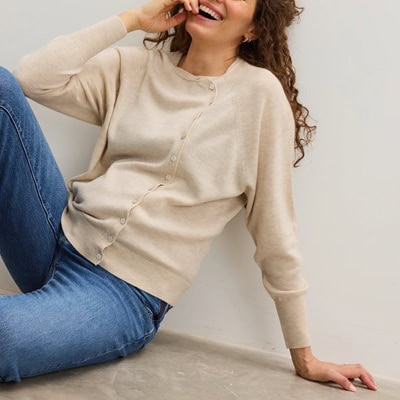 A woman wearing blue jeans and an oatmeal-colored cardigan