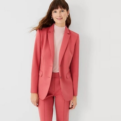 A woman with long brown hair wearing a dark pink blazer and suit pants and a off-white blouse