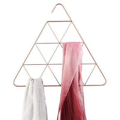 A gold-tone, metal, triangular hanging scarf organizer with gray and pink scarves on it