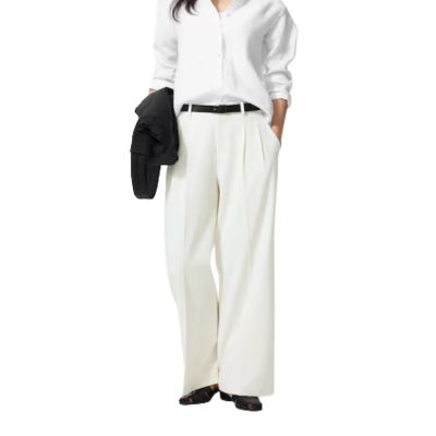 Woman in white blouse and wide-leg trousers holding a blazer. and a white blouse. She is carrying a black jacket
