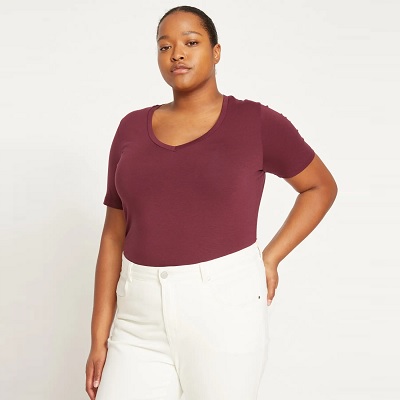 A woman with black hair pulled back and wearing a burgundy shirt and white pants