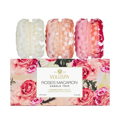 Three macaron-shaped candles (ivory, peach, and pink) on top of a floral box labeled Voluspa Roses Macaron Candle Trio