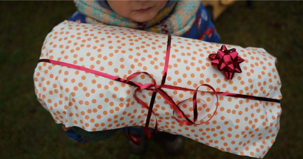 A light-skinned child (face mostly cropped out) holding a wrapped gift with a ribbon and bow