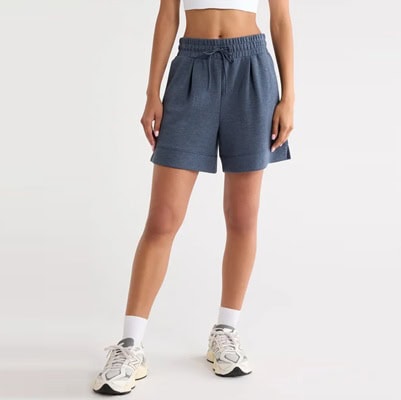 A woman wearing white sneakers, white socks, a white crop top, and blueish-gray athletic shorts
